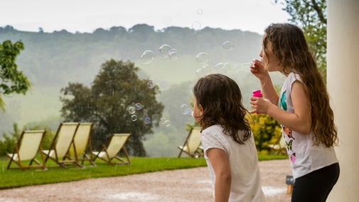 Two young visitors blowing bubbles in the rain outside the house at Greenway, looking out over the deckchairs in the garden